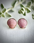 Pink scallop shell earrings on a white fabric background with greenery