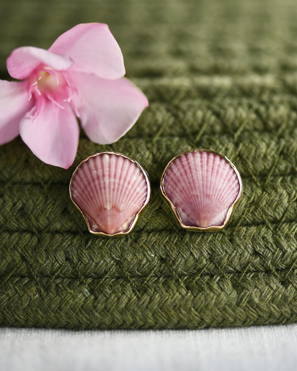 Pink shell earrings on a green textured surface with a pink flower.