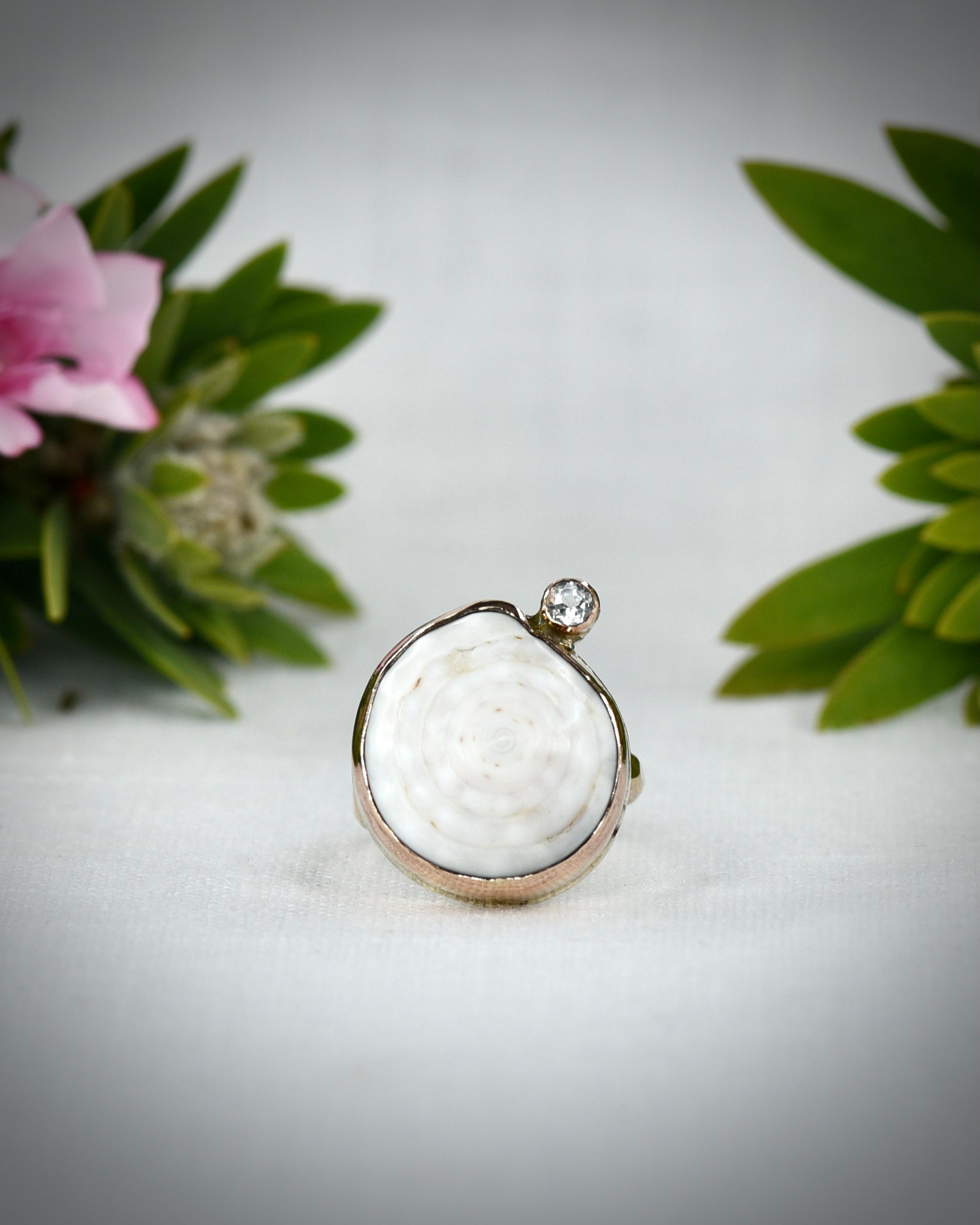 Close view of a pale Hawaiian puka shell ring displayed among tropical flowers