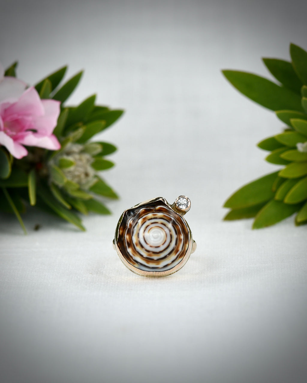 Front view of brown and cream Hawaiian puka shell ring displayed among tropical flowers
