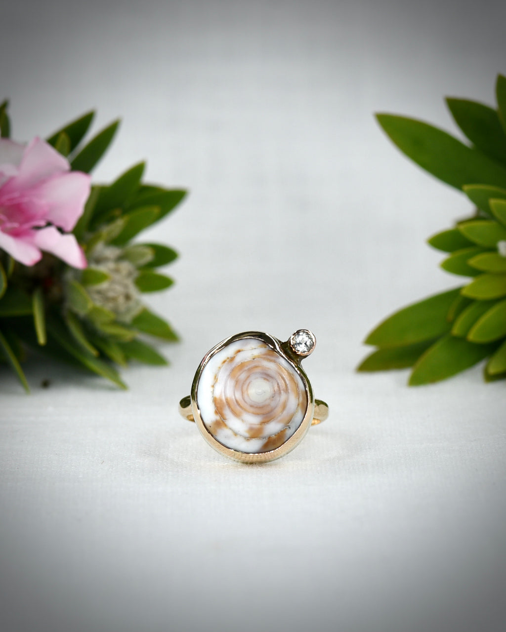 Front view of cream and brown Hawaiian puka shell ring displayed among tropical flowers
