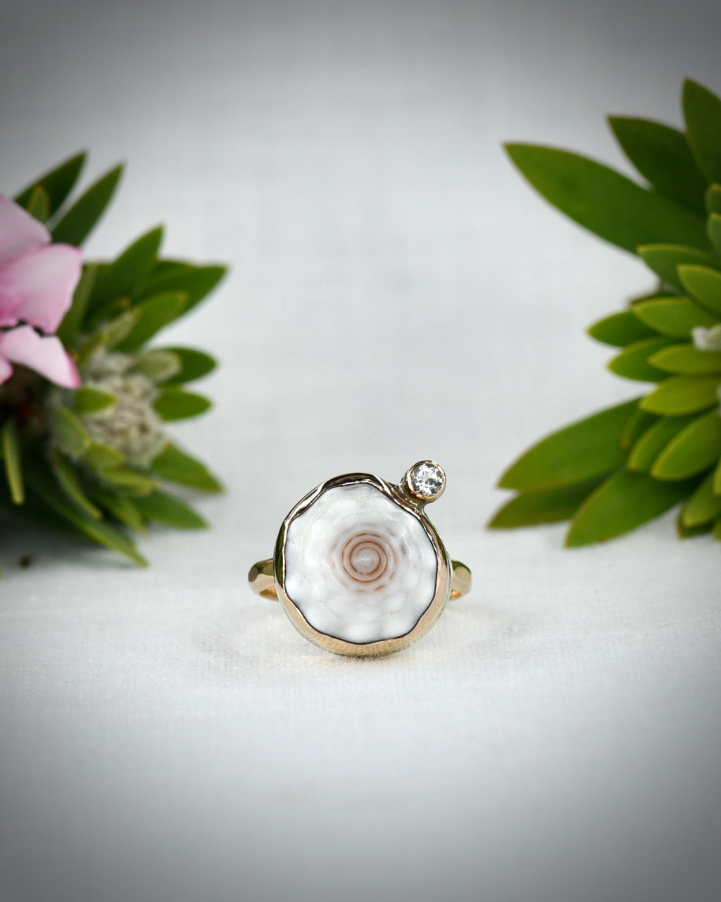 Front view of pale cream Hawaiian puka shell ring displayed among tropical flowers
