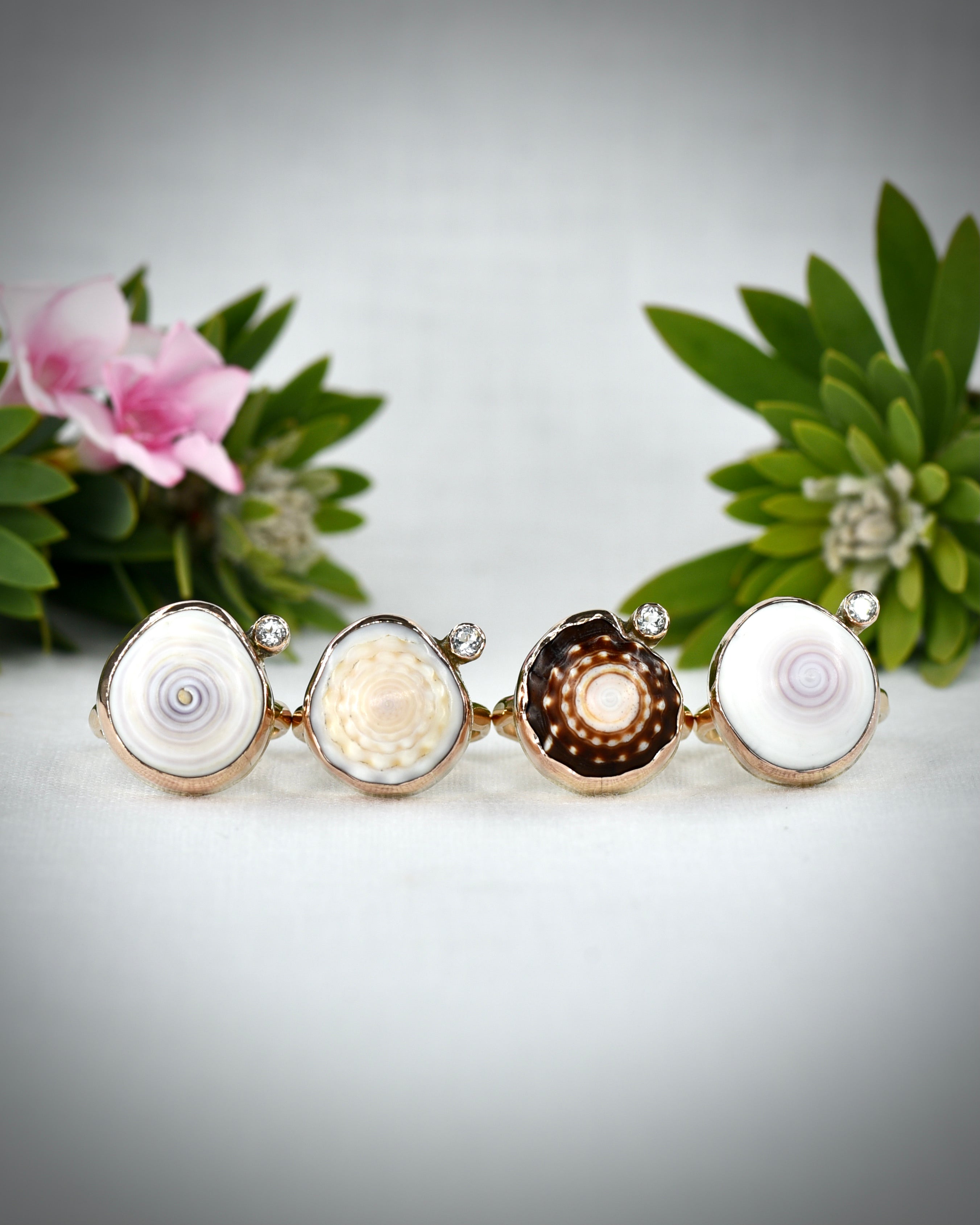 Four natural Hawaiian puka shell and topaz rings in size 7 displayed together among tropical flowers