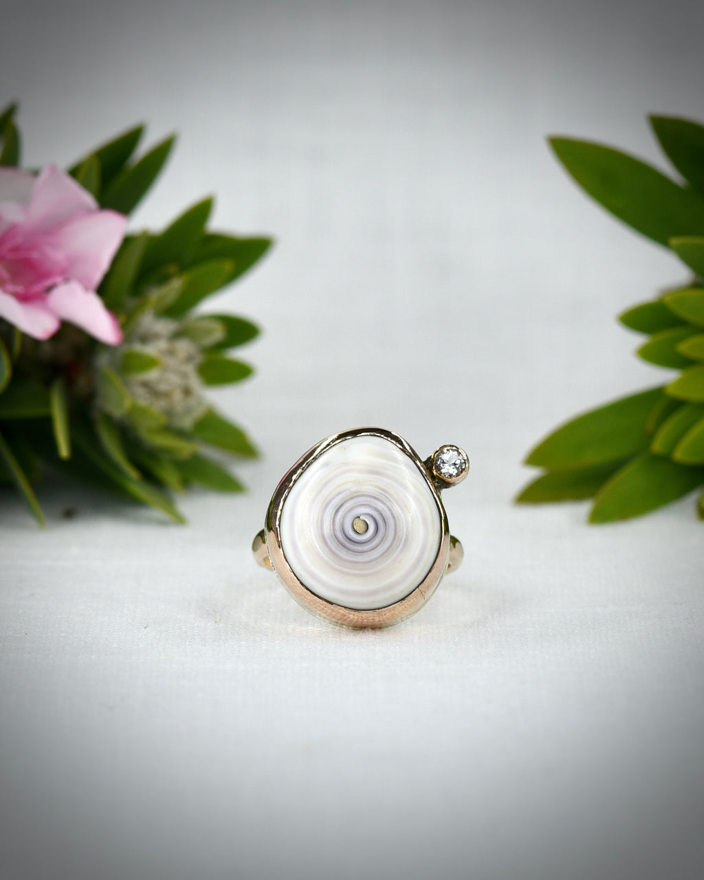 Front view of pale purple Hawaiian puka shell ring displayed among tropical flowers