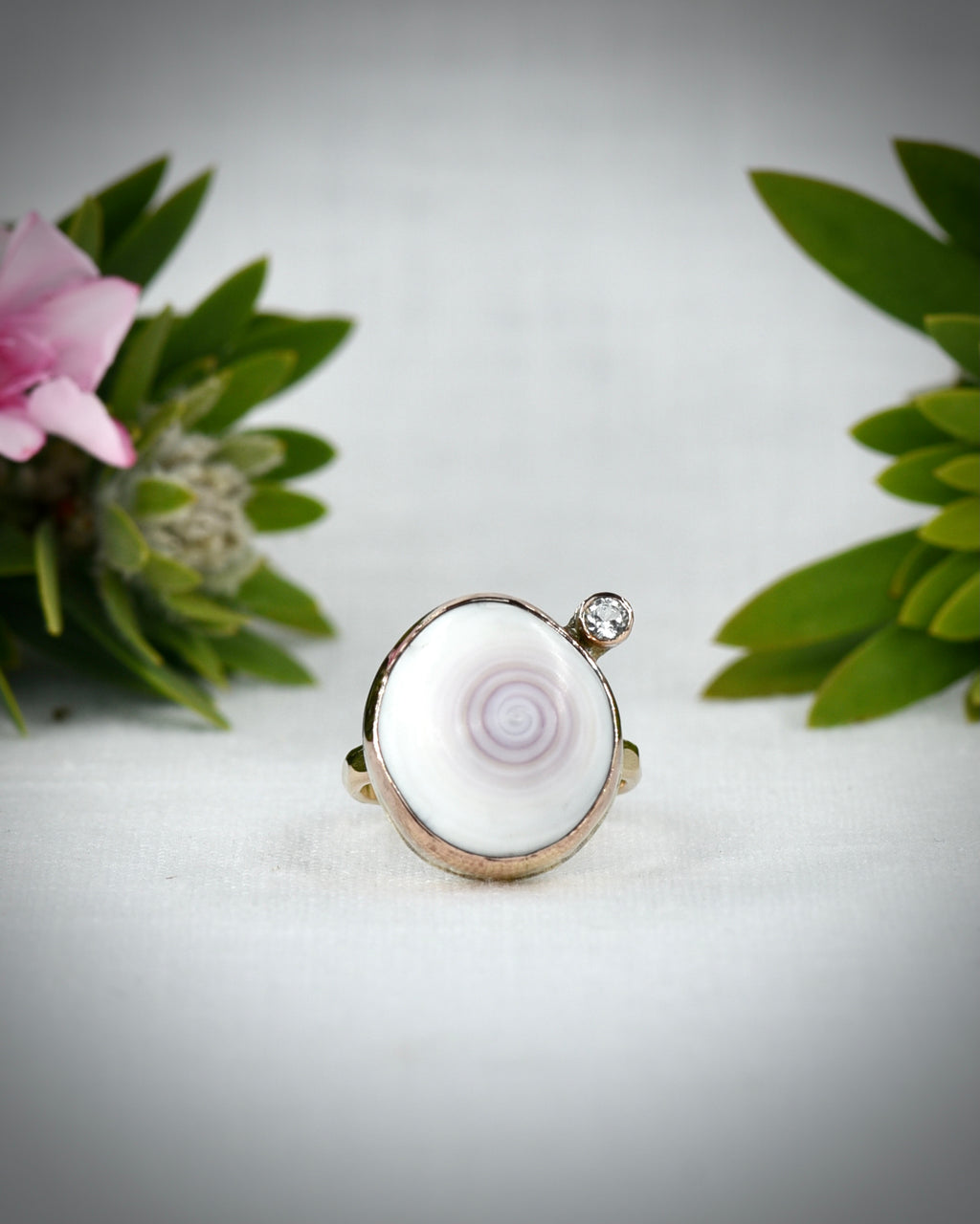 Front view of white Hawaiian puka shell ring displayed among tropical flowers
