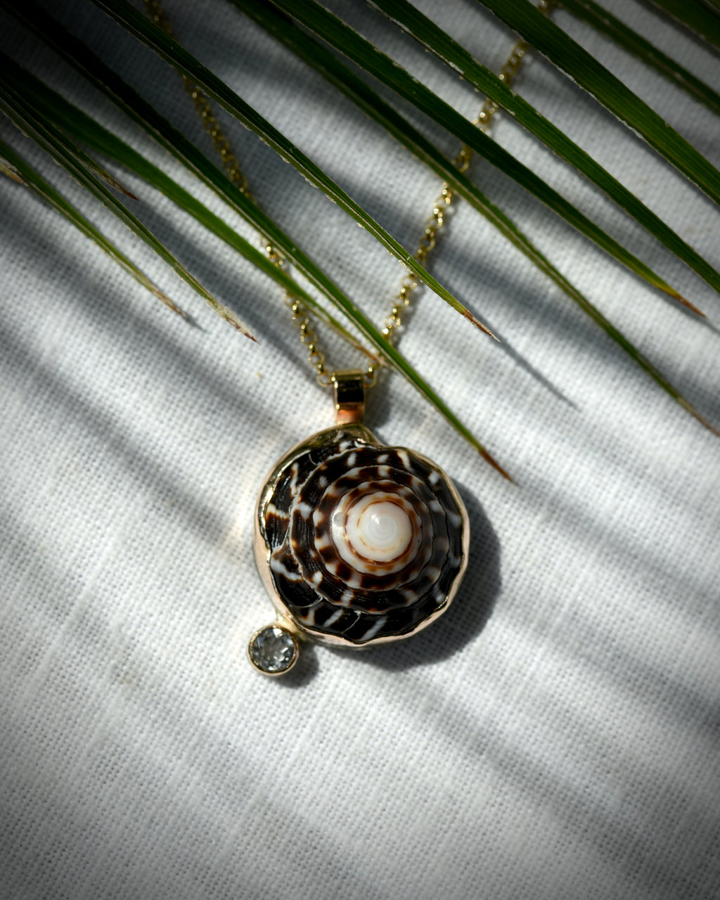 Close view of dark brown and cream Hawaiian puka shell and topaz Midi Puka Dot necklace displayed beneath palm leaves
