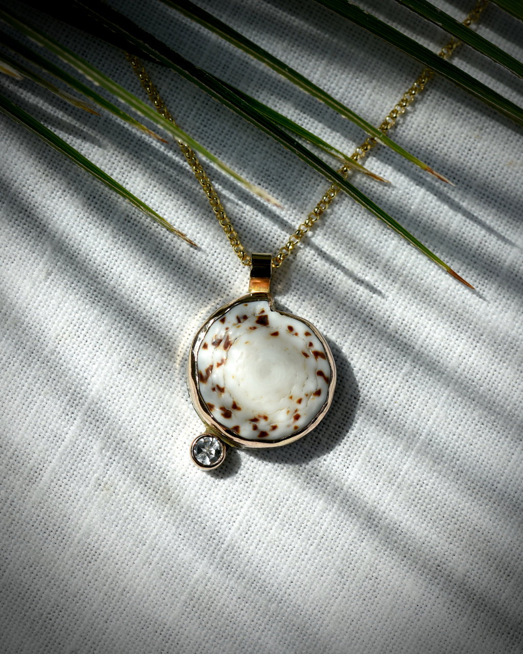 Close view of cream and brown Hawaiian puka shell and topaz Midi Puka Dot necklace displayed beneath palm leaves
