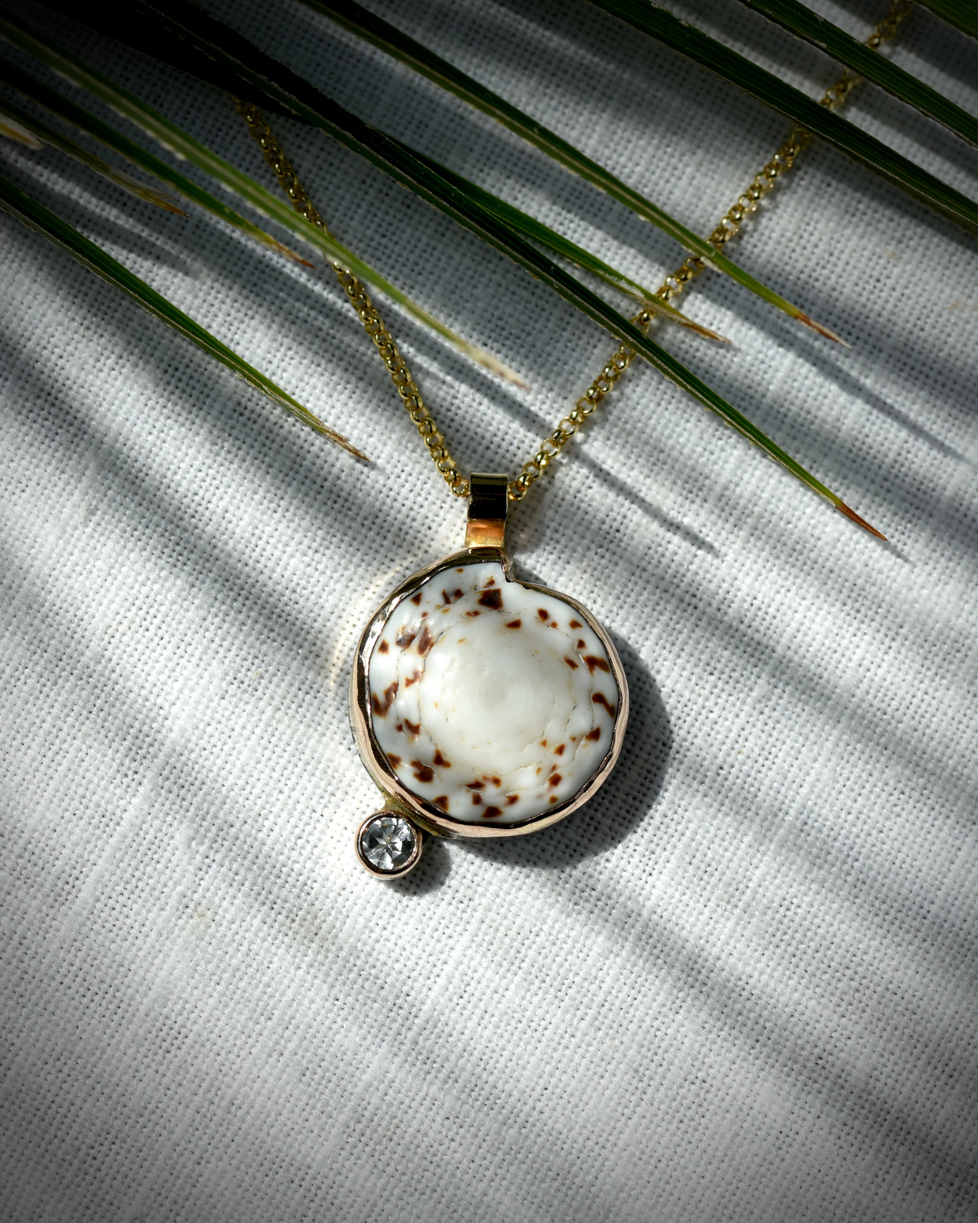 Close view of cream and brown Hawaiian puka shell and topaz Midi Puka Dot necklace displayed beneath palm leaves
