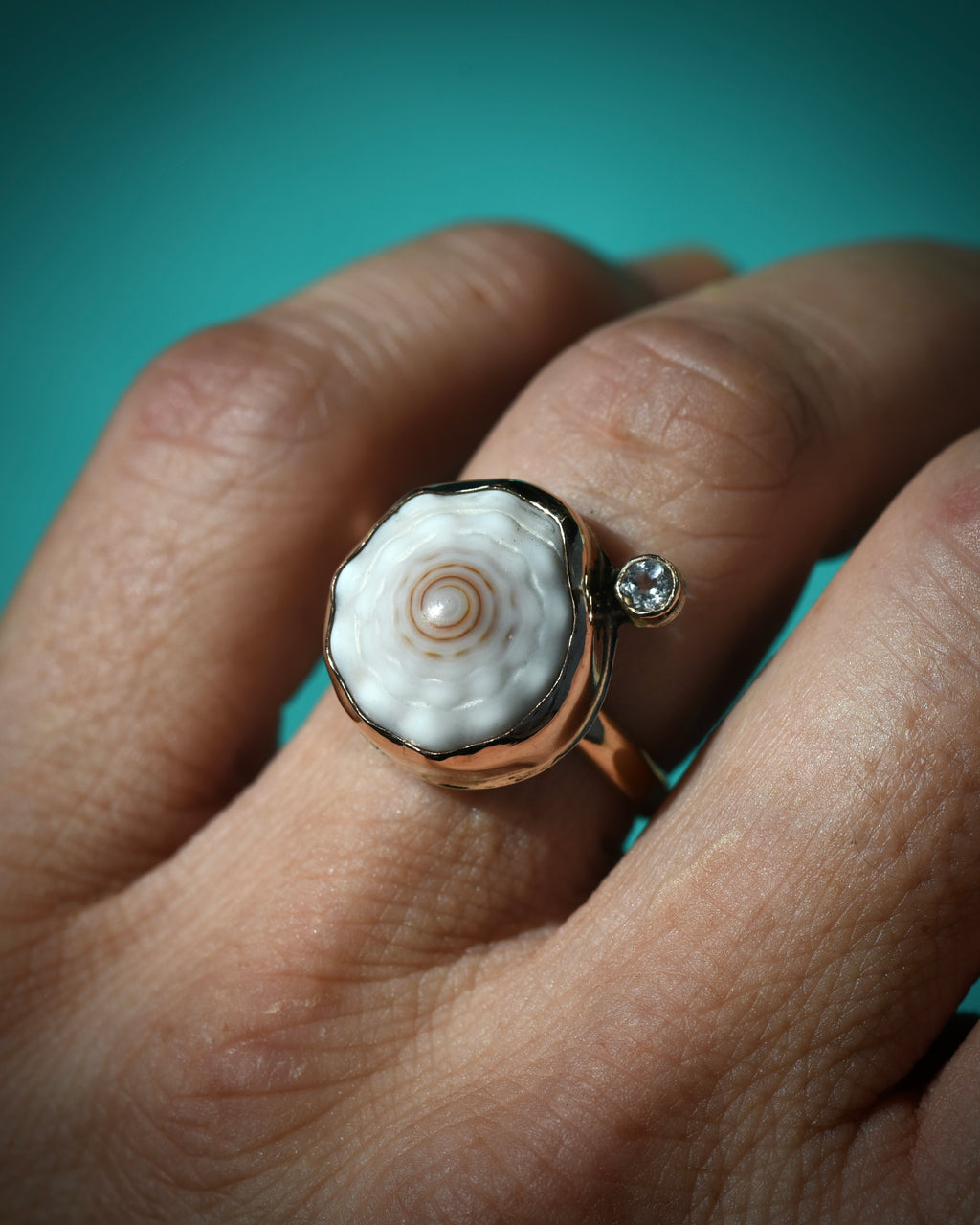 Pale cream Hawaiian puka shell ring worn on the finger, showing the centered white topaz accent