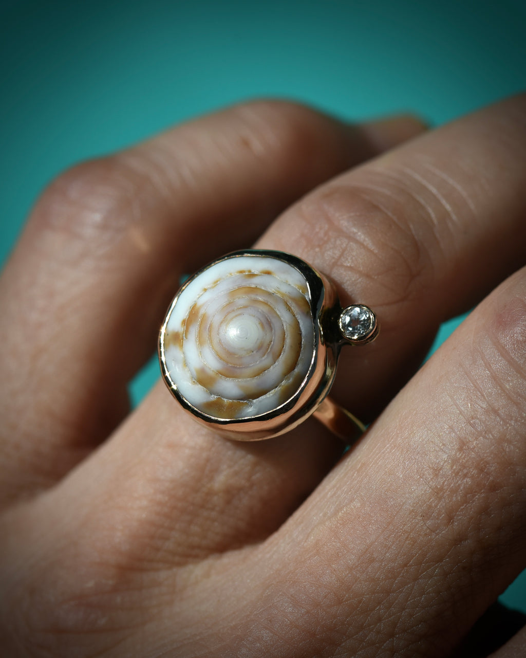 Cream and brown Hawaiian puka shell ring worn on the finger, showing the natural concentric shell pattern