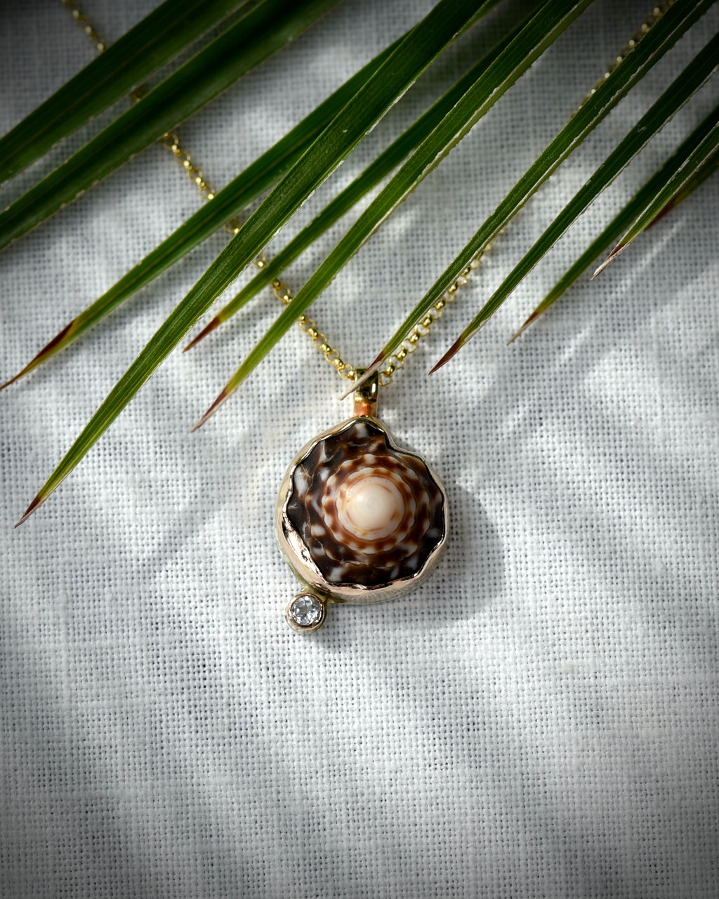 Close view of dark brown and cream Hawaiian puka shell and topaz Petite Puka Dot necklace displayed beneath palm leaves
