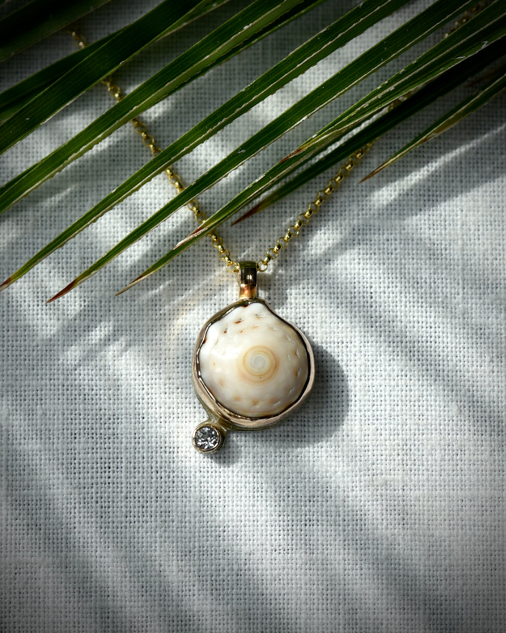 Close view of cream and tan Hawaiian puka shell and topaz Petite Puka Dot necklace displayed beneath palm leaves
