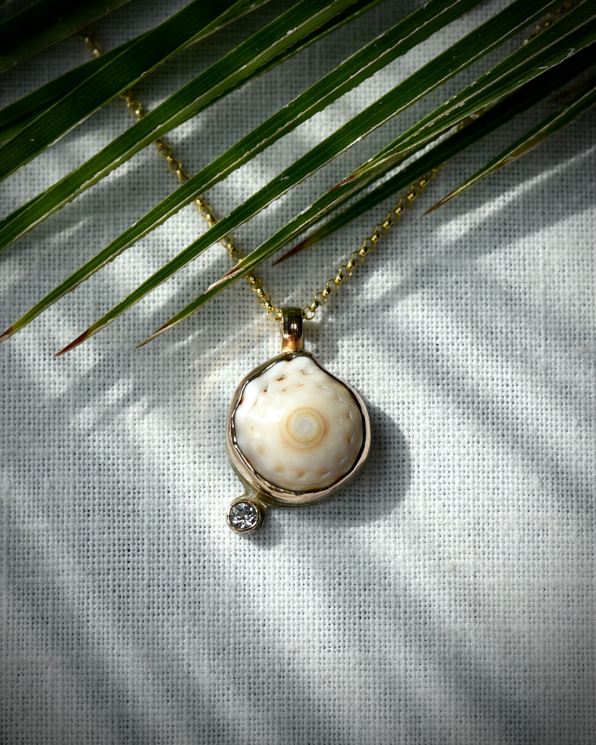 Close view of cream and tan Hawaiian puka shell and topaz Petite Puka Dot necklace displayed beneath palm leaves
