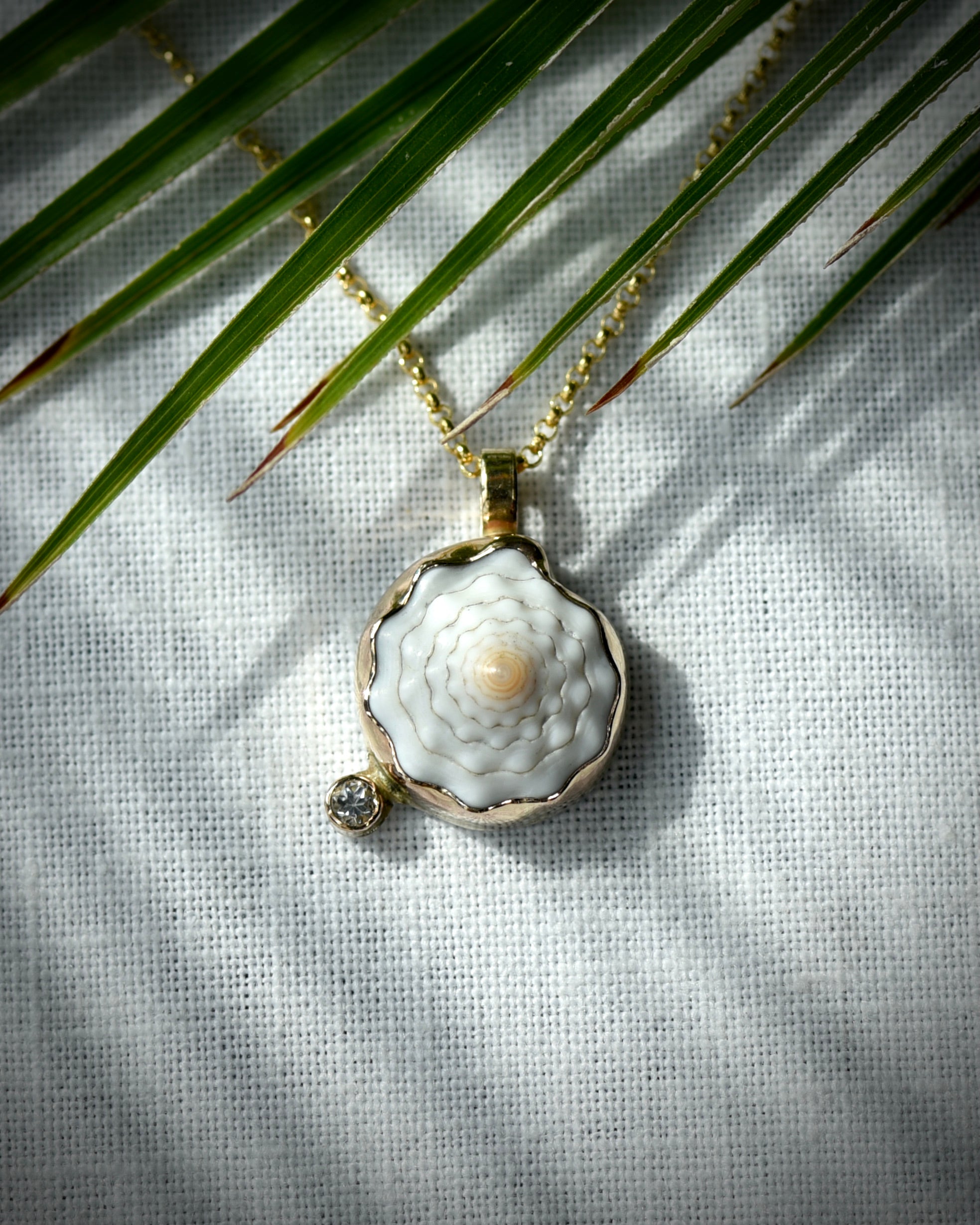 Close view of pale cream Hawaiian puka shell and topaz Petite Puka Dot necklace displayed beneath palm leaves