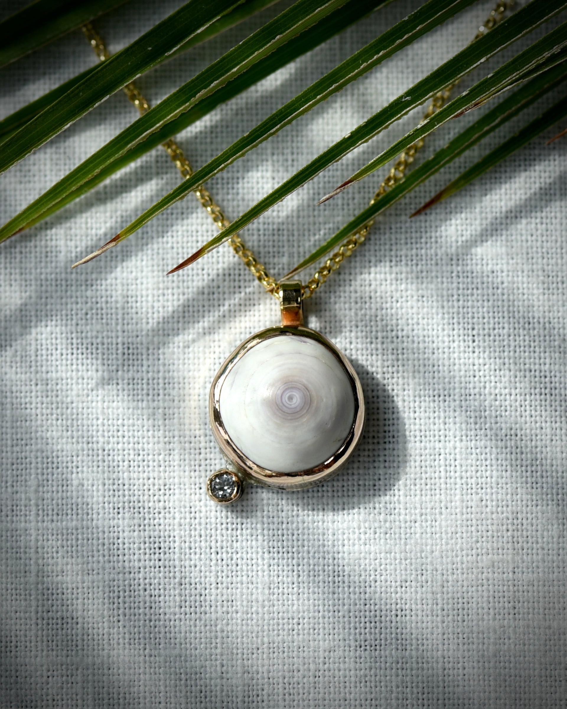 Close view of pale purple Hawaiian puka shell and topaz Petite Puka Dot necklace displayed beneath palm leaves