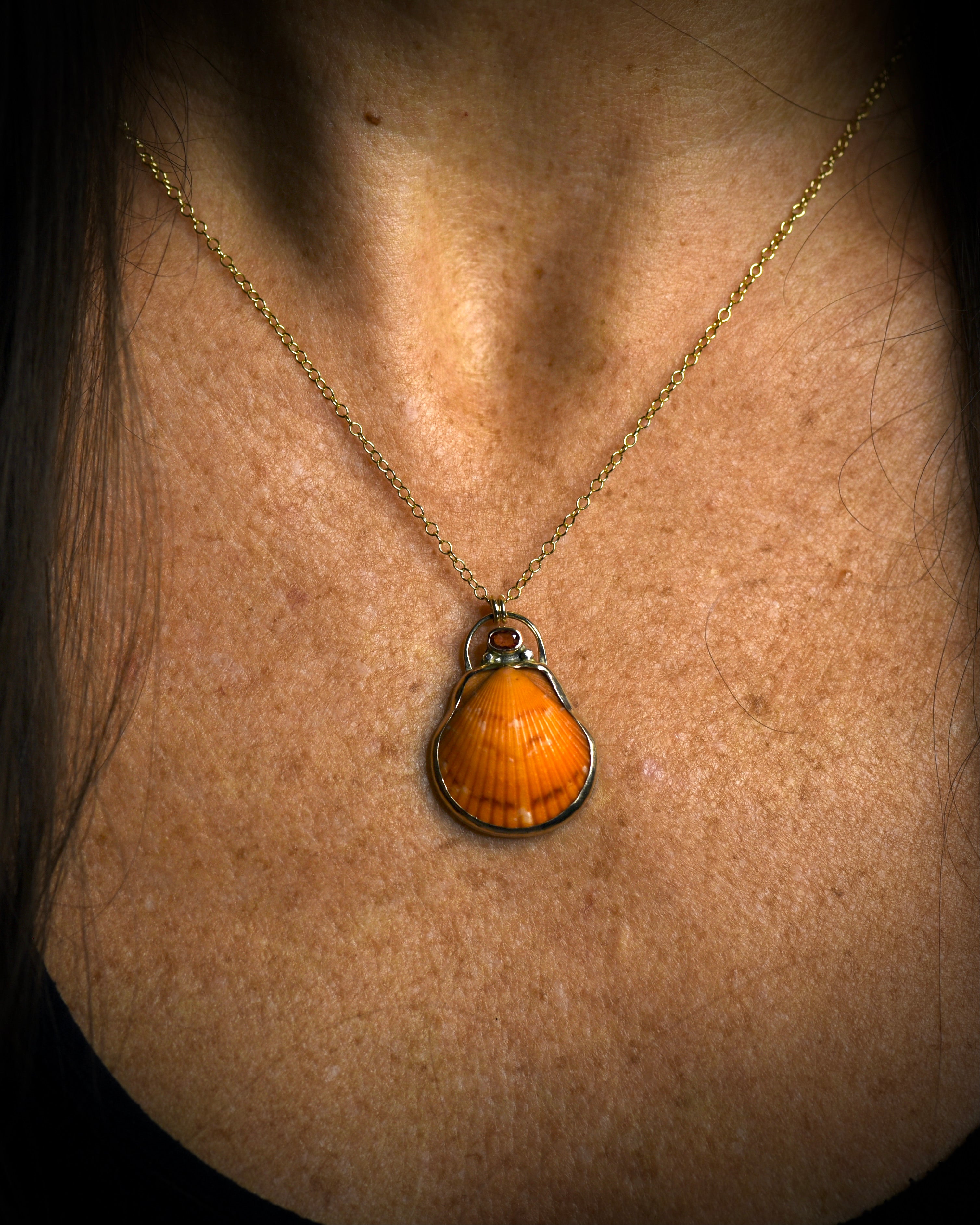 Orange scallop shell pendant necklace worn on a delicate chain