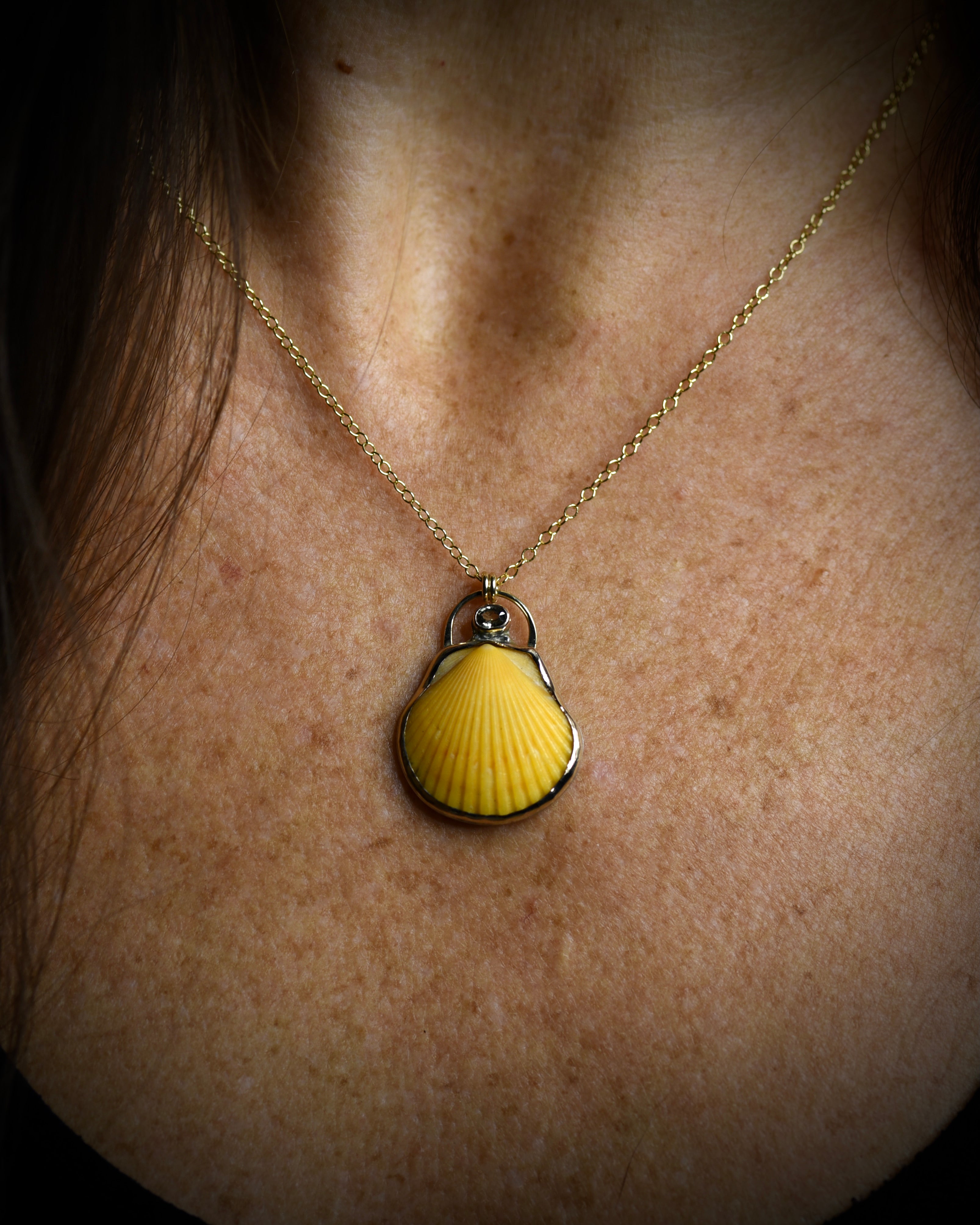Yellow scallop shell pendant necklace worn on a delicate chain