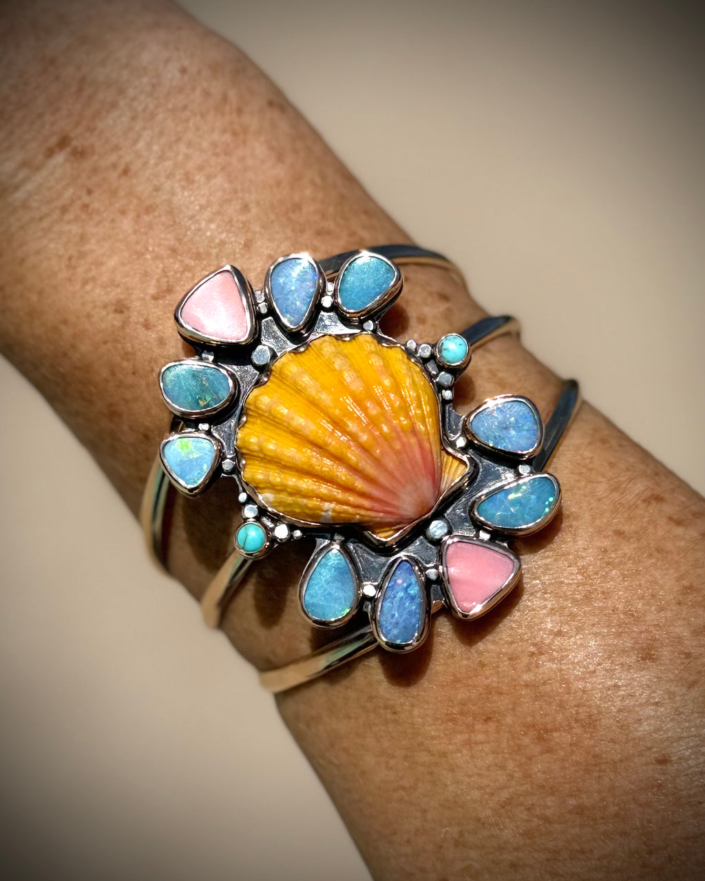 Reef Riot cuff worn on the wrist, showing the bright sunrise shell and colorful gemstone setting
