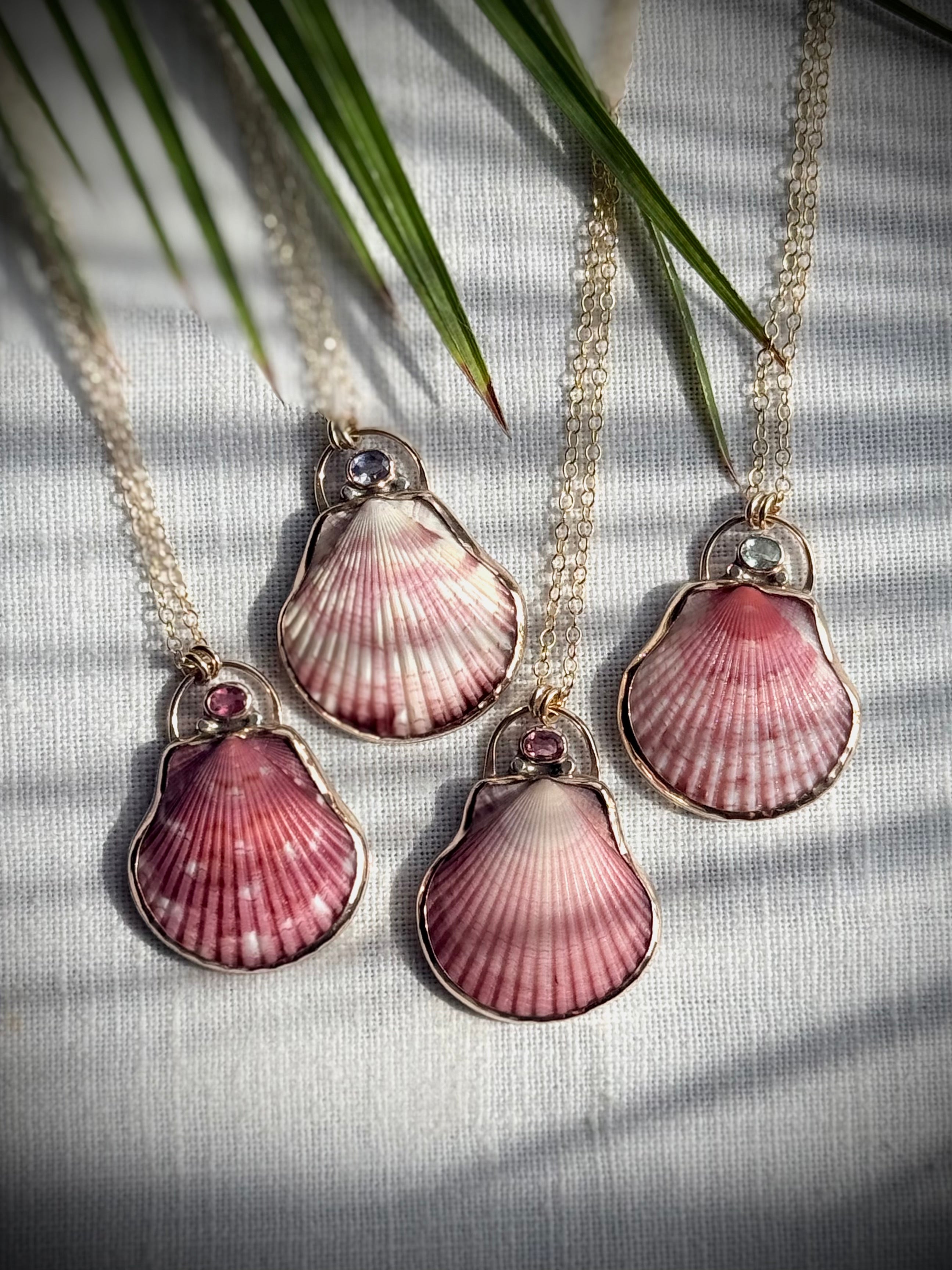 Four pink scallop shell pendant necklaces displayed side by side
