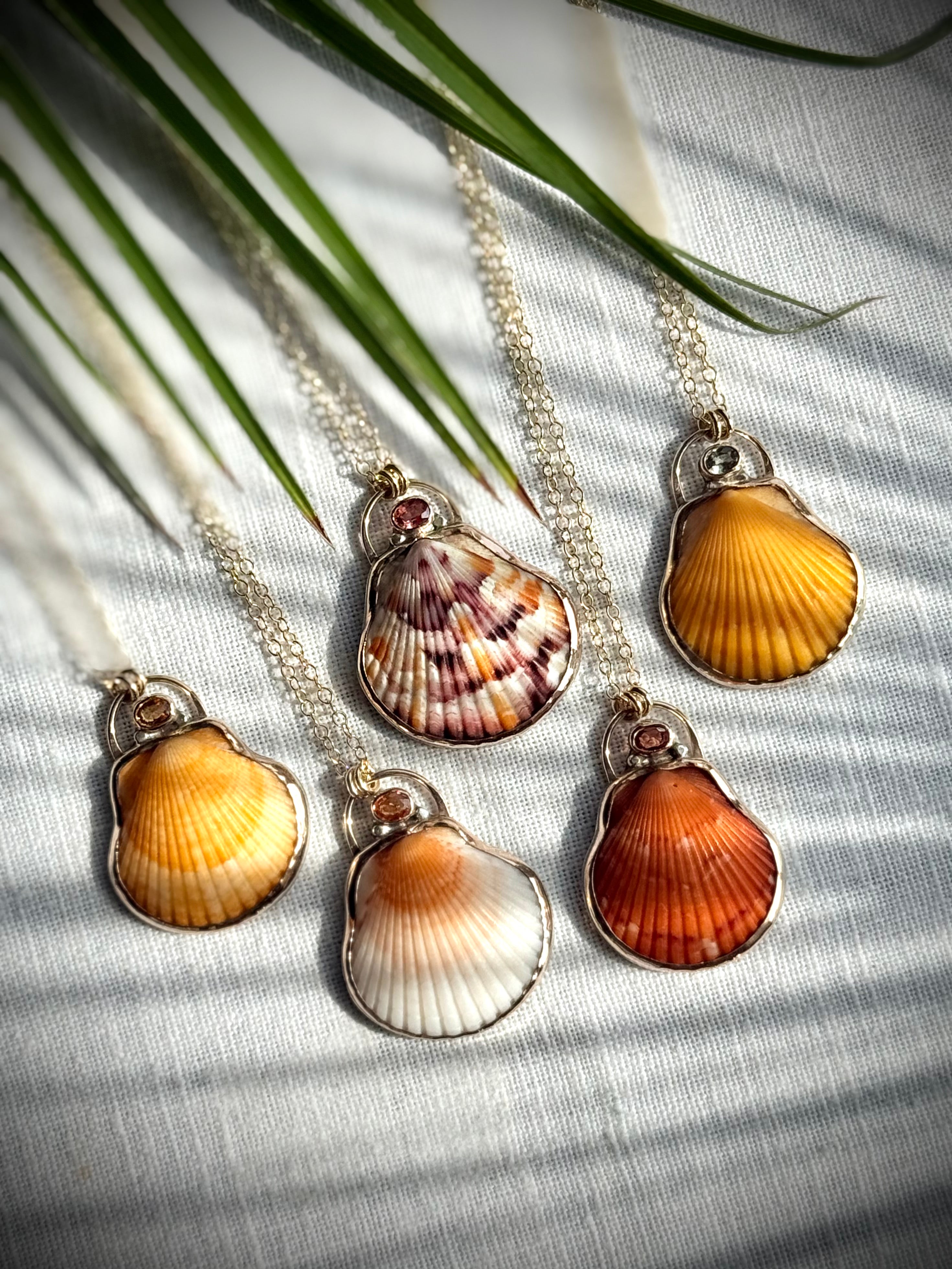 Assortment of orange, cream, and patterned scallop shell pendant necklaces displayed together

